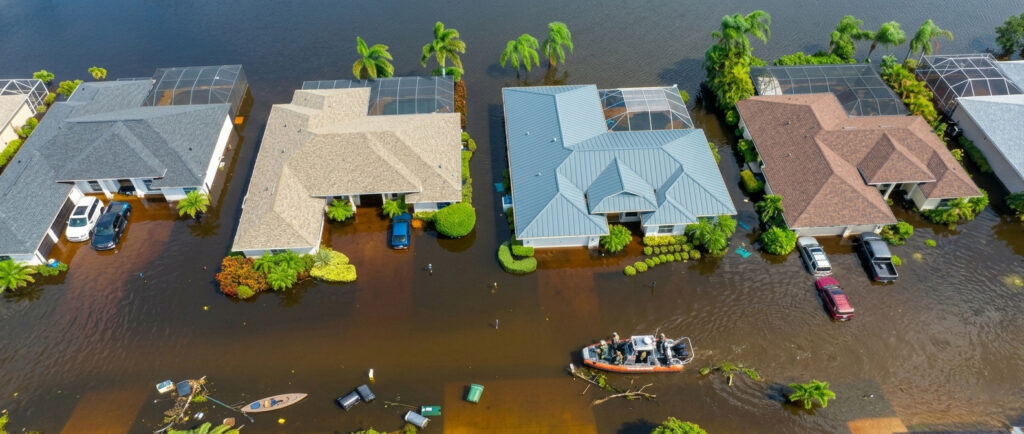 An aerial view of a flooded neighborhood with homes surrounded by floodwater and a rescue boat navigating the street, the risk flood insurance florida covers.