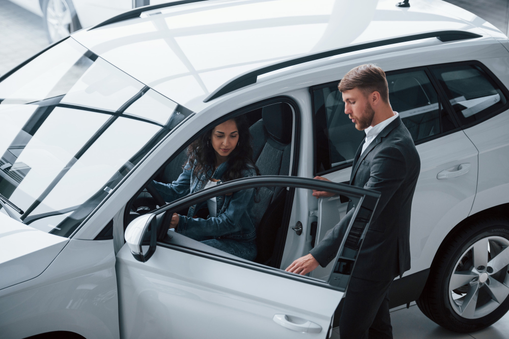 A salesperson helping a woman into the driver's seat of a new white SUV at a dealership, representing a driver preparing for Auto Insurance Florida.
