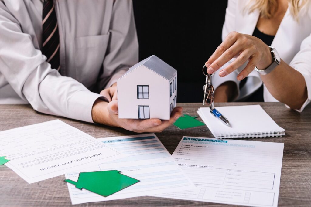 Two investors exchanging house keys over mortgage application paperwork and a model home, reflecting a Real Estate Investor Insurance Florida property purchase.