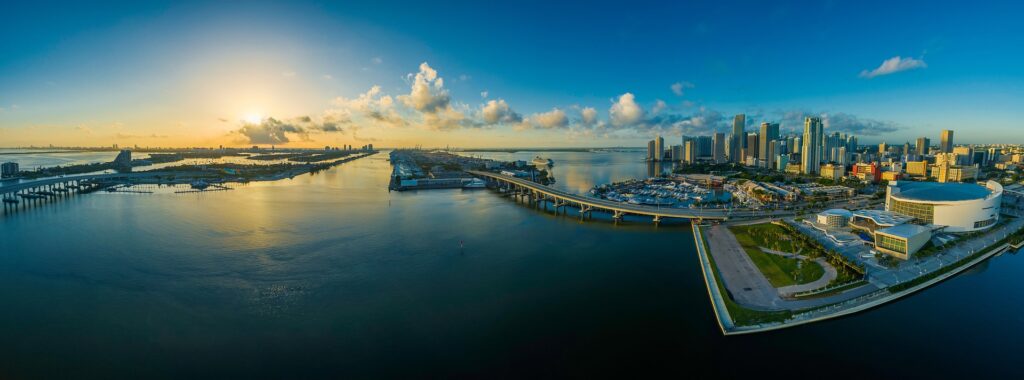 An aerial panorama of a Miami waterway with a bridge, marina, and downtown skyline at sunrise, the coastal property Waterfront Property Insurance covers.
