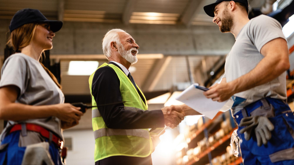 A supervisor in a safety vest shaking hands with a warehouse worker holding a clipboard, the kind of business Workers Compensation Insurance Florida protects.