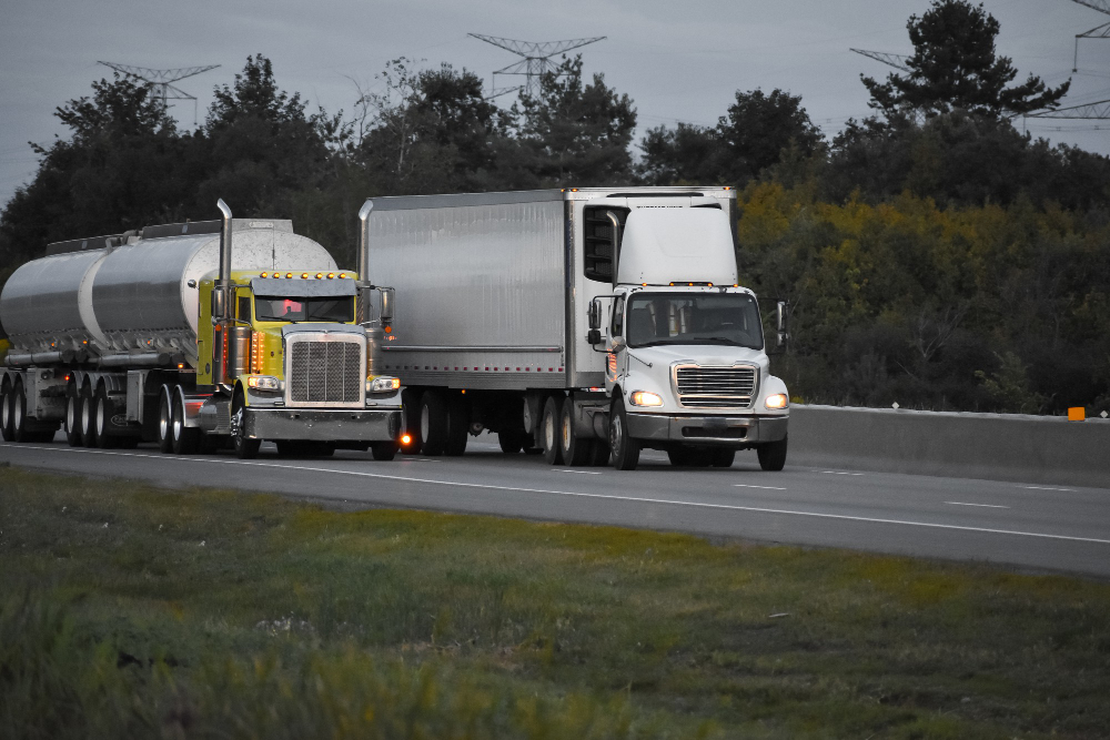 Two commercial trucks driving on a Florida highway at dusk, illustrating a 3A Allied Insurance blog article on commercial vehicle coverage risks