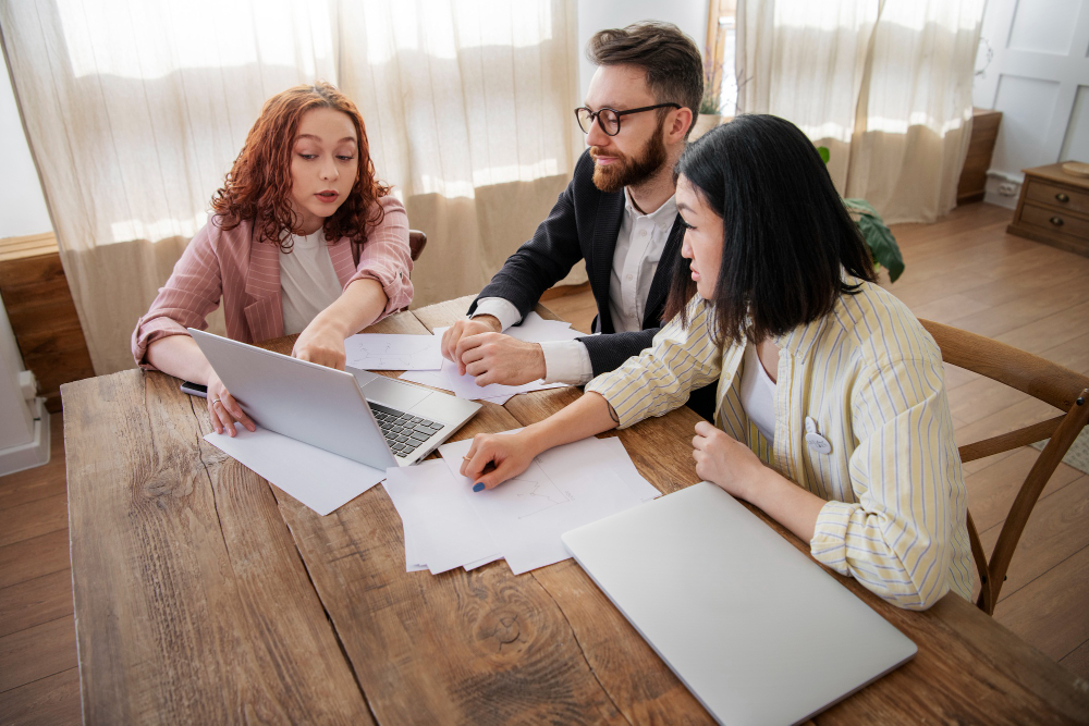 A small group reviews paperwork and laptops together at a wooden table, reflecting the Personal Insurance coverage guidance, 3A Allied provides clients.